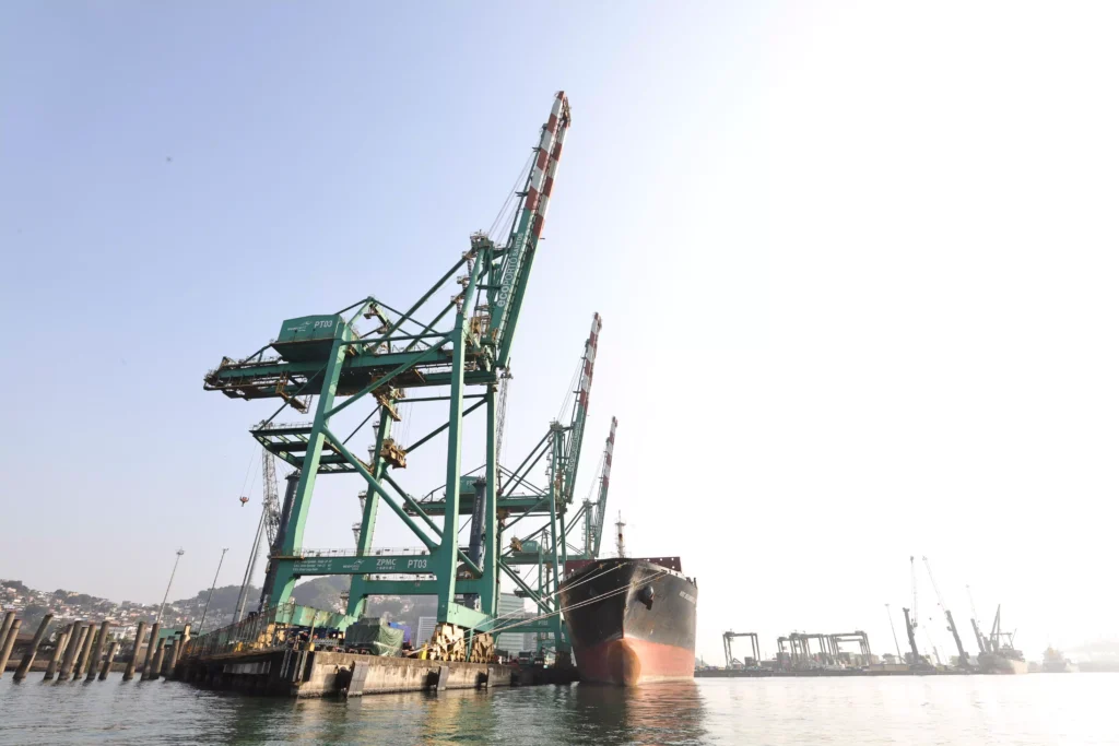 Imagem de um porto com guindastes de carga e um navio atracado, em uma área portuária industrial, destacando infraestrutura marítima moderna.