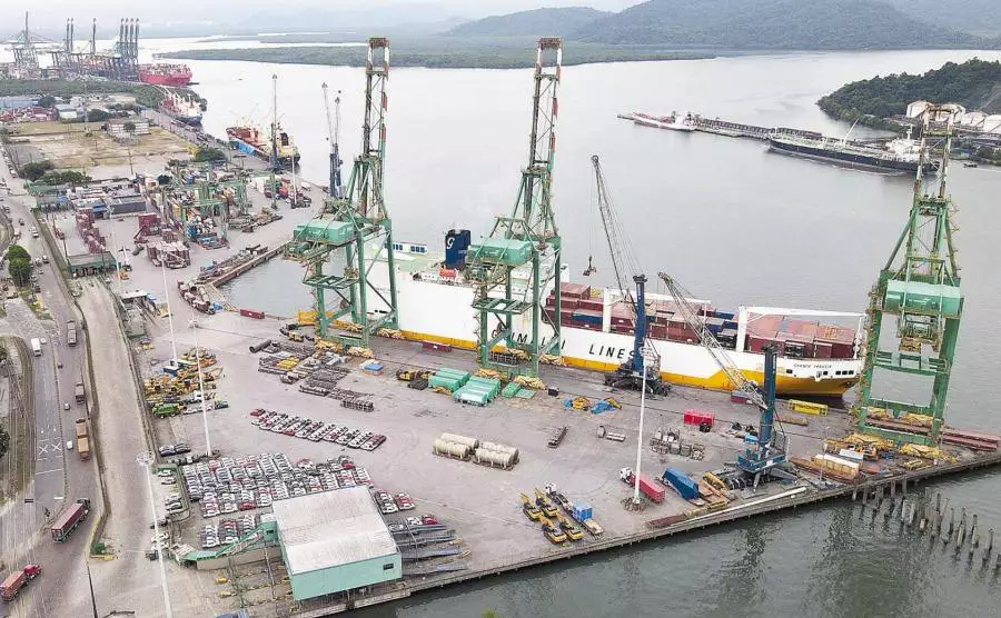Vista panorâmica do porto com navio cargueiro e guindastes de movimentação de carga, destacando a atividade de transporte marítimo e logística no Brasil.