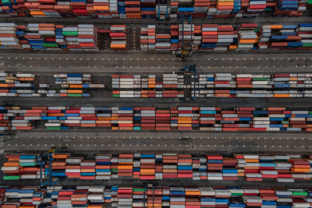 Imagem aérea de um pátio de transporte de containers coloridos, mostrando várias fileiras organizadas com diferentes cores em um ambiente industrial.