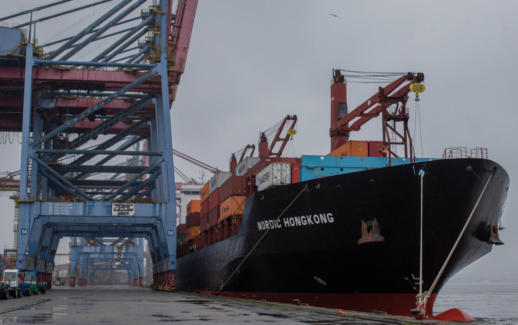 Caminhão de carga e navio de carga no porto com contêineres e guindastes, movimentando mercadorias de transporte marítimo e rodoviário para comércio internacional.