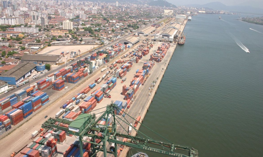 Imagem aérea do Porto de Santos com contêineres de carga e terminal de transporte fluvial, destacando a importância da logística e transporte marítimo no Brasil.