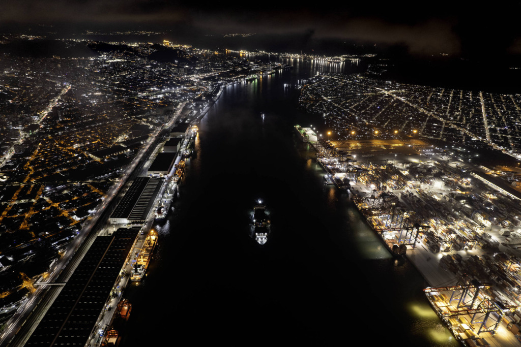 Vista noturna de Santos com grande ponte sobre o rio, iluminada por luzes urbanas e refletindo a movimentação da cidade à noite.