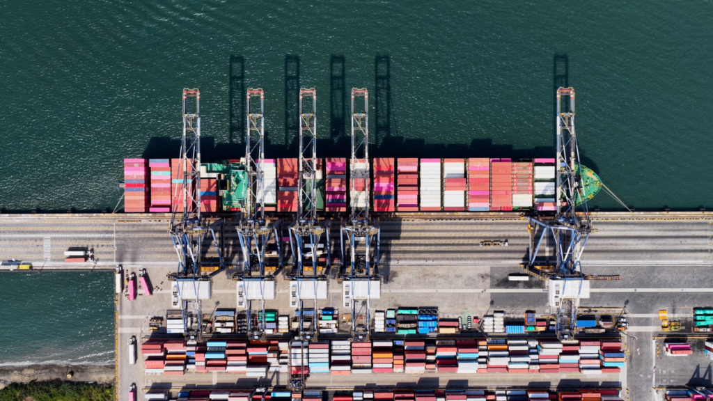 Imagem aérea do Porto de Santos com várias plataformas de containers e guindastes, destacando a operação de exportação e importação no terminal marítimo.